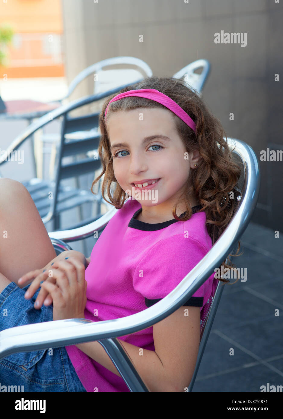 Smiling girl sitting in outdoor aluminium silver chair and pink t-shirt Stock Photo