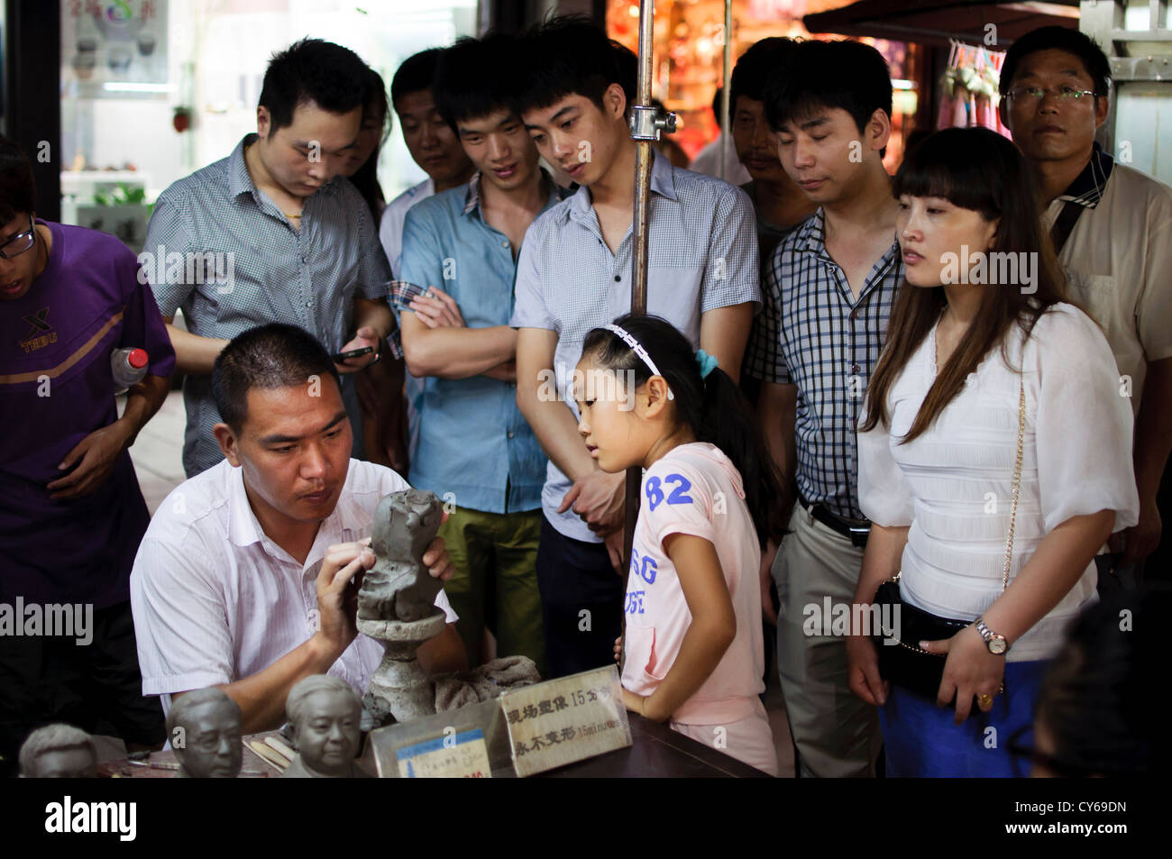 A man moulds a clay figure head on Qinghefang Old Street, Hangzhou, whilst bystanders look on Stock Photo
