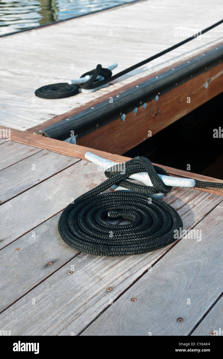 Black ropes coiled on a wooden dock and tied to a metal dock cleats