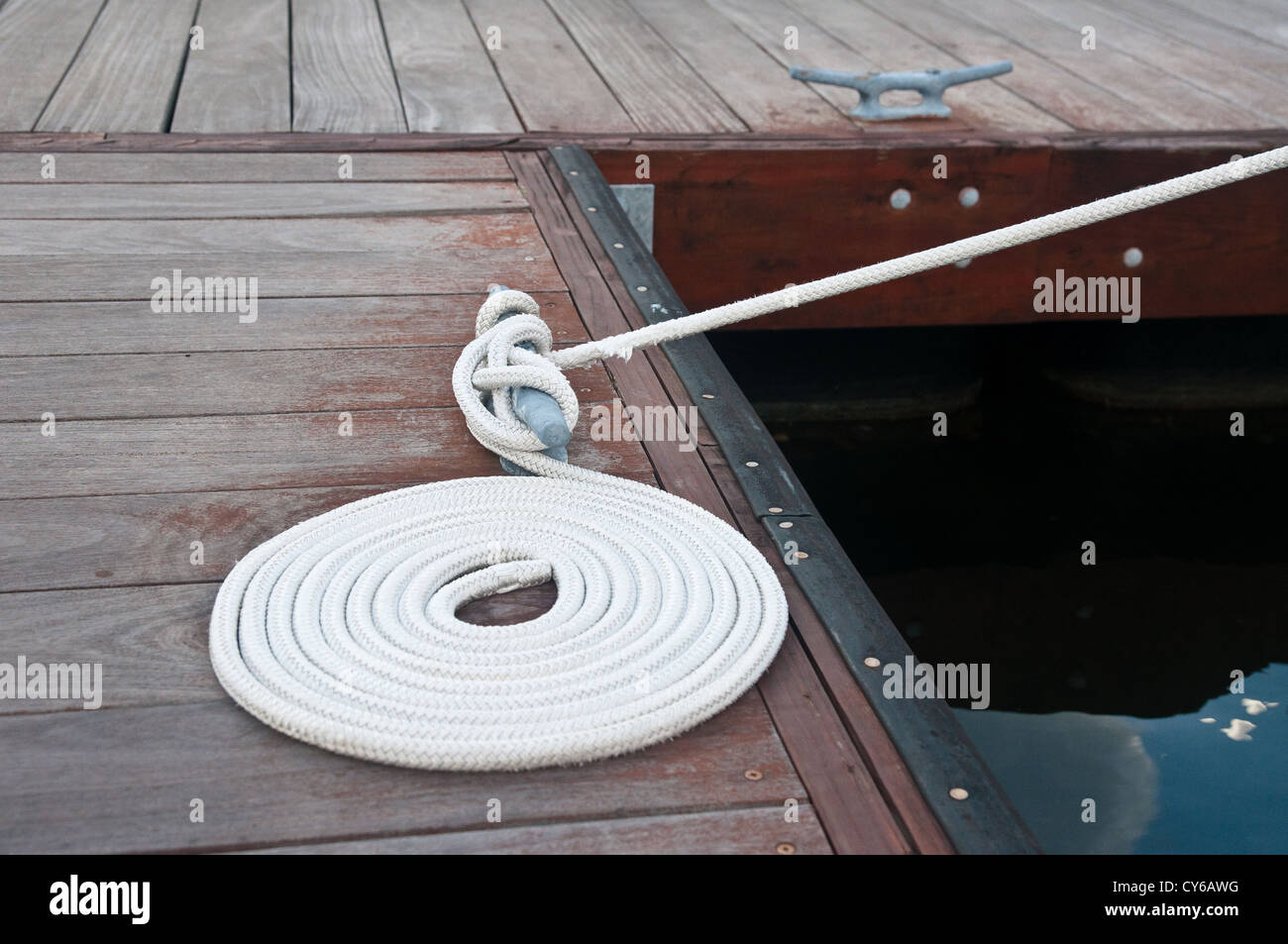 White rope coiled on a wooden dock and tied to a metal dock cleat