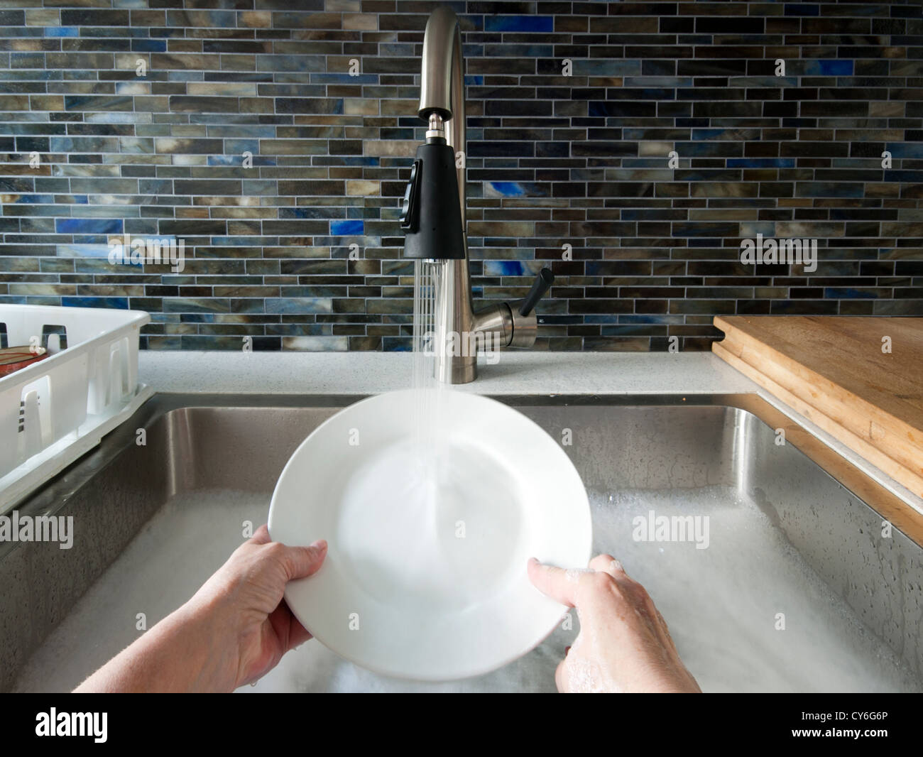 Hands in kitchen sink with soapy water washing the dishes by hand Stock