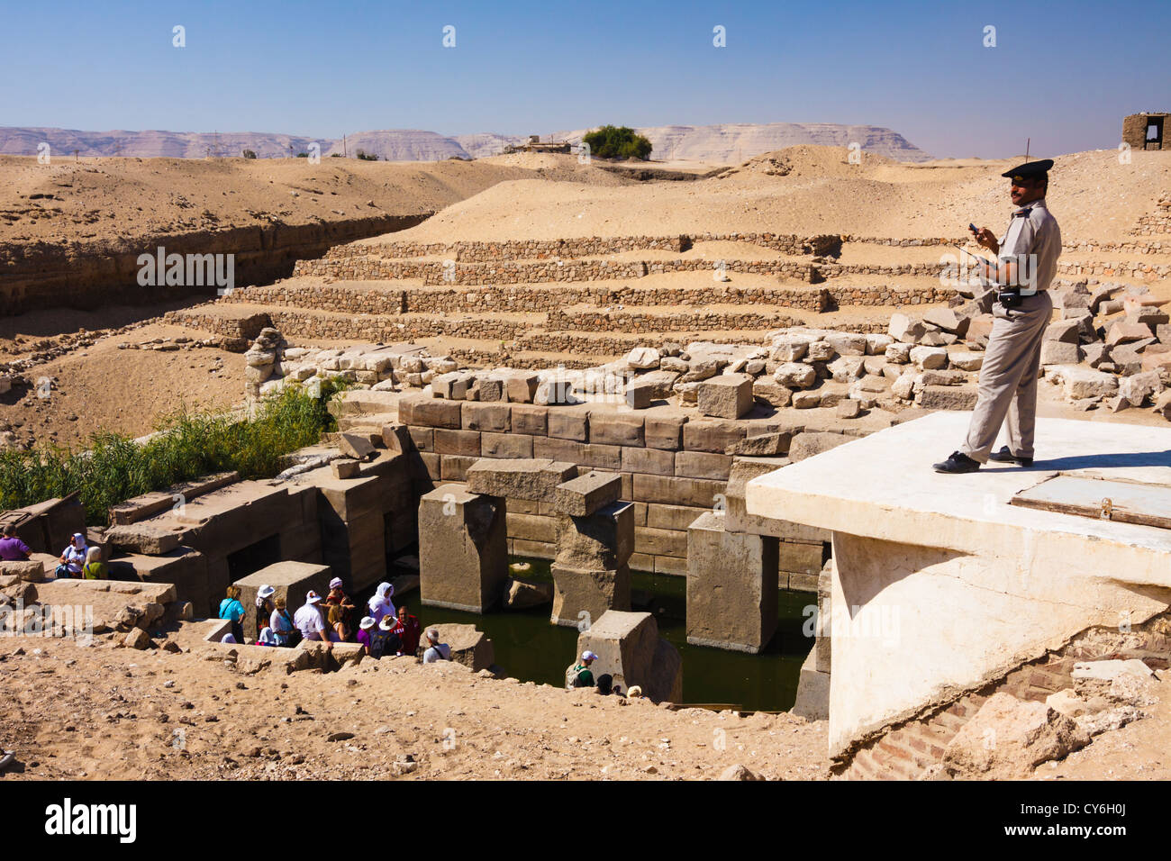 Egyptian policeman watching a sightseeing tour visiting the submerged Osireion cenotaph at Abydos, Al-Balyana, Egypt Stock Photo