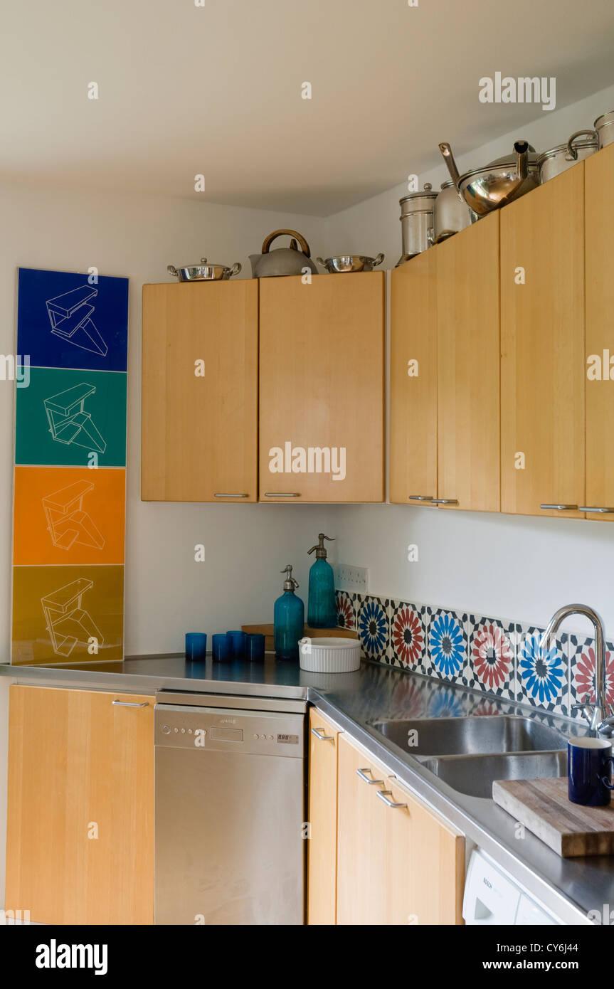 Wood fitted kitchen with stainless steel worktop and brightly coloured artwork Stock Photo