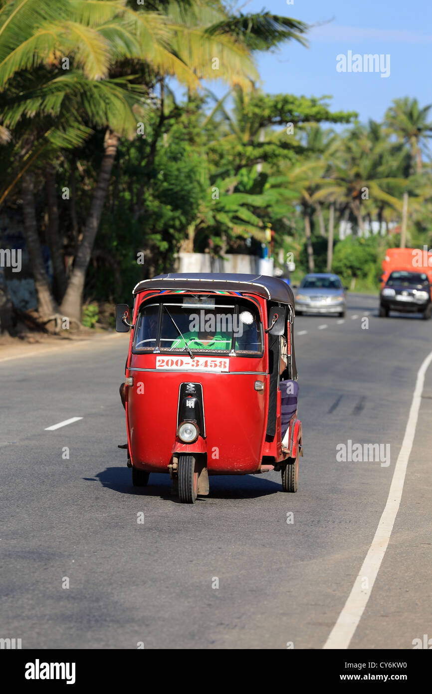 Red tuk tuk driving along the main coastal road at Koggala in Sri Lanka. Stock Photo