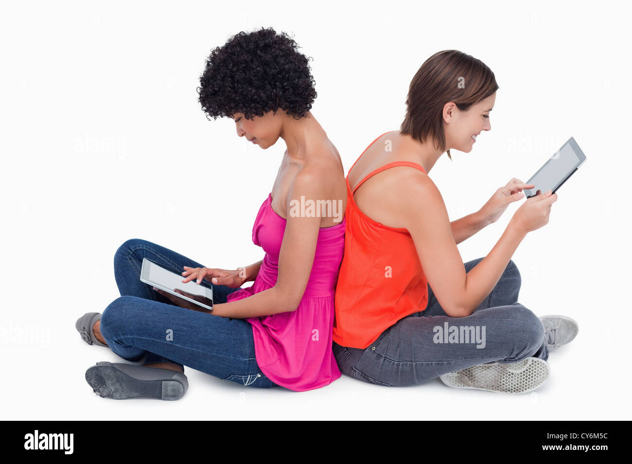 Teenage girl holding her tablet PC in the air while a friend is hers putting her on legs Stock Photo