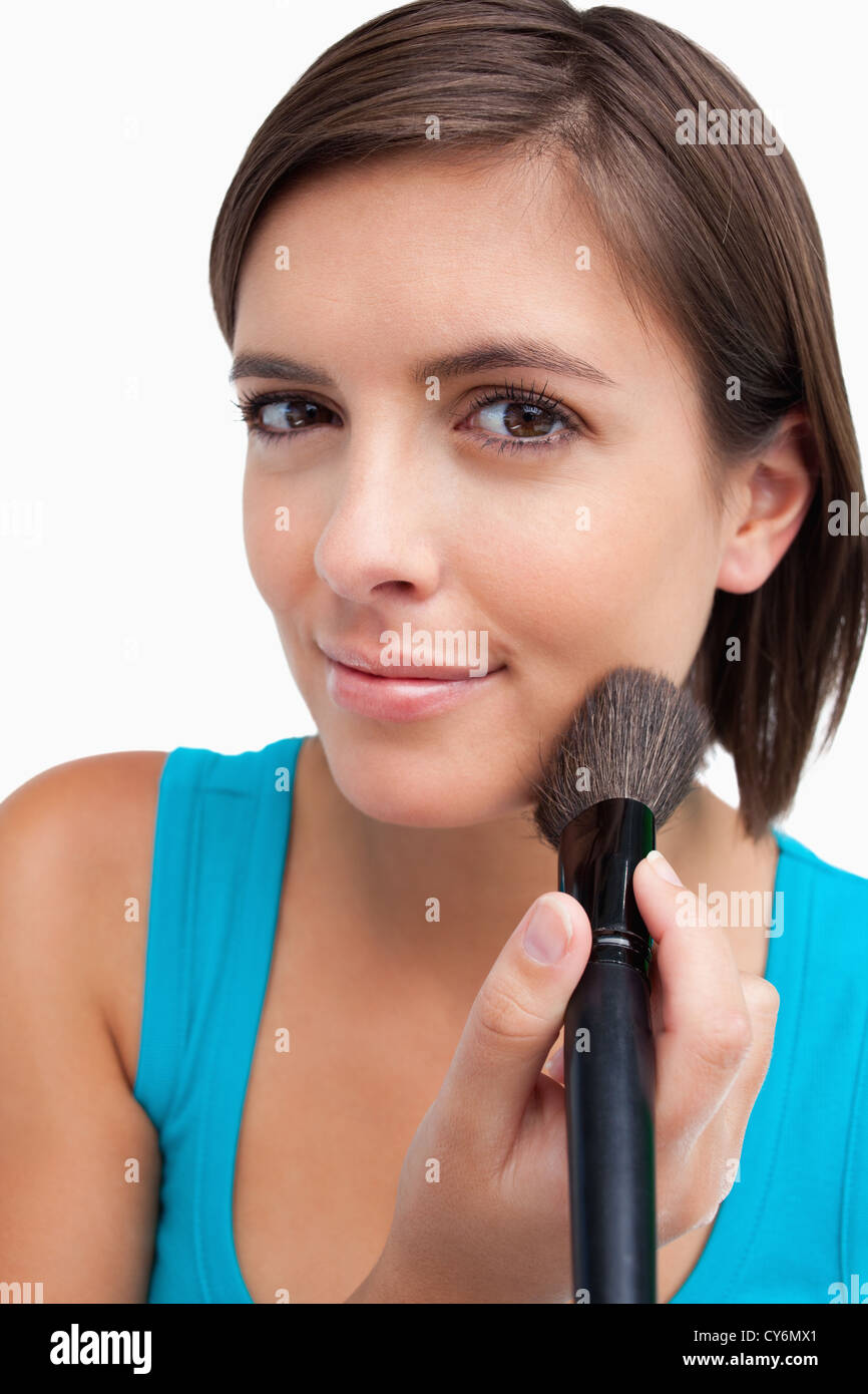 Attractive teenager standing upright while applying make-up with a powder brush Stock Photo
