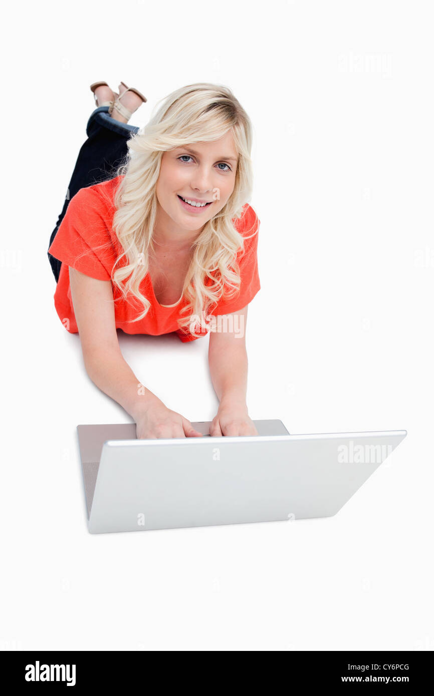 Smiling attractive woman using her laptop while lying on the floor ...