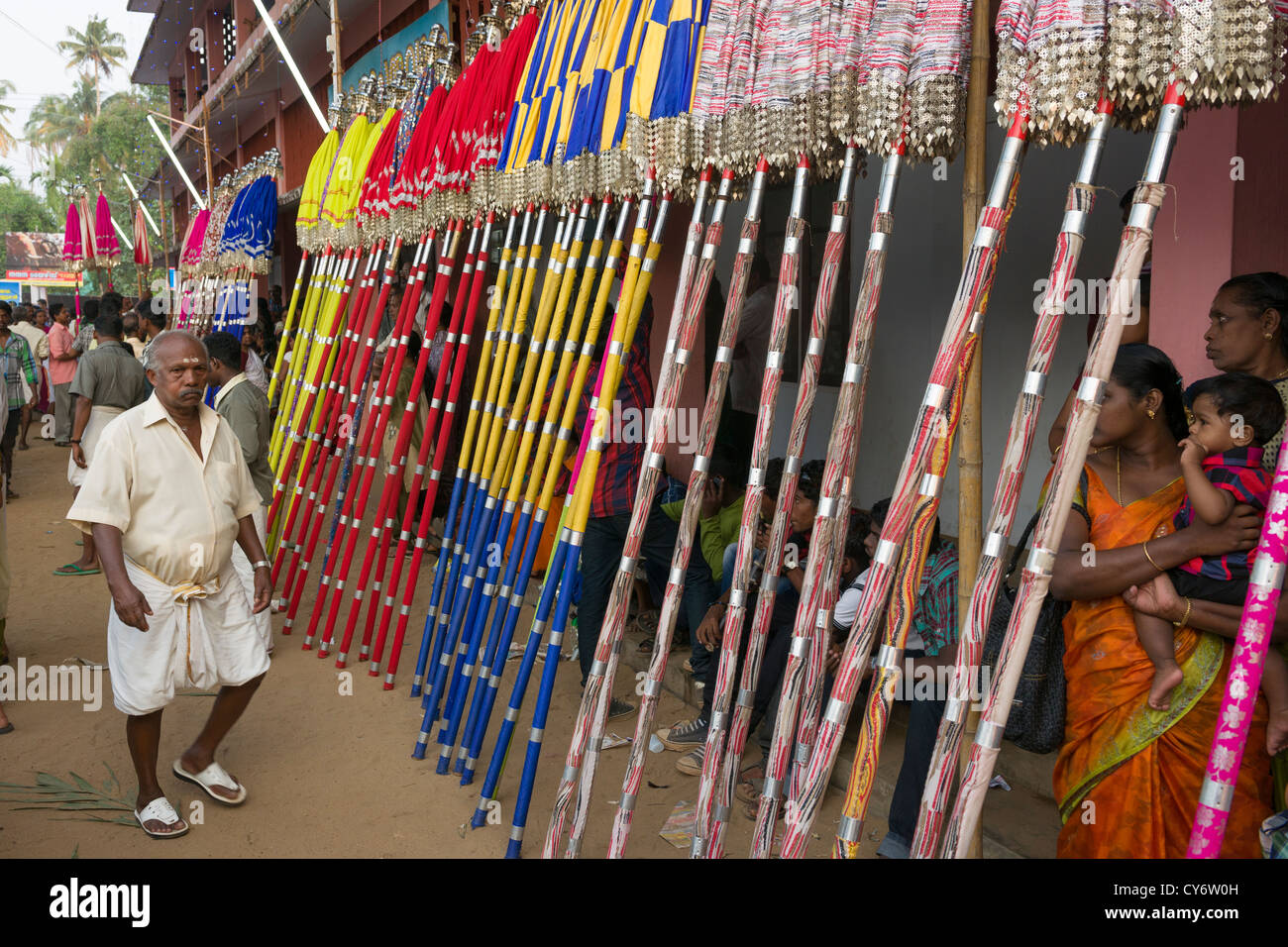 Pilgrim walking past coloured parasols called Muthukuda lined up for the Goureeswara Temple Festival, Cherai, near Kochi (Cochin), Kerala, India Stock Photo