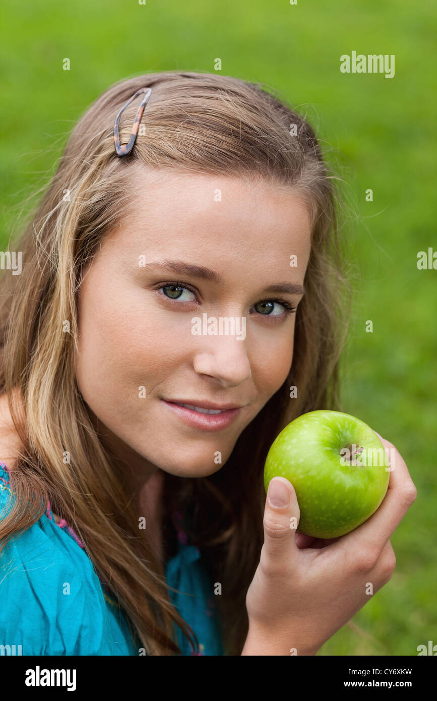 Attractive young girl holding a delicious green apple while standing in a park Stock Photo