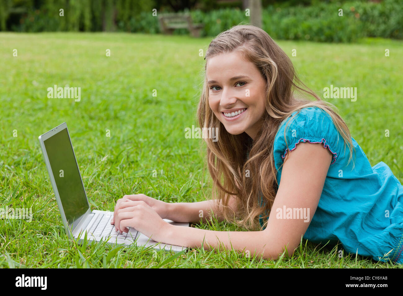 Smiling teenager using her laptop while lying down in a park Stock