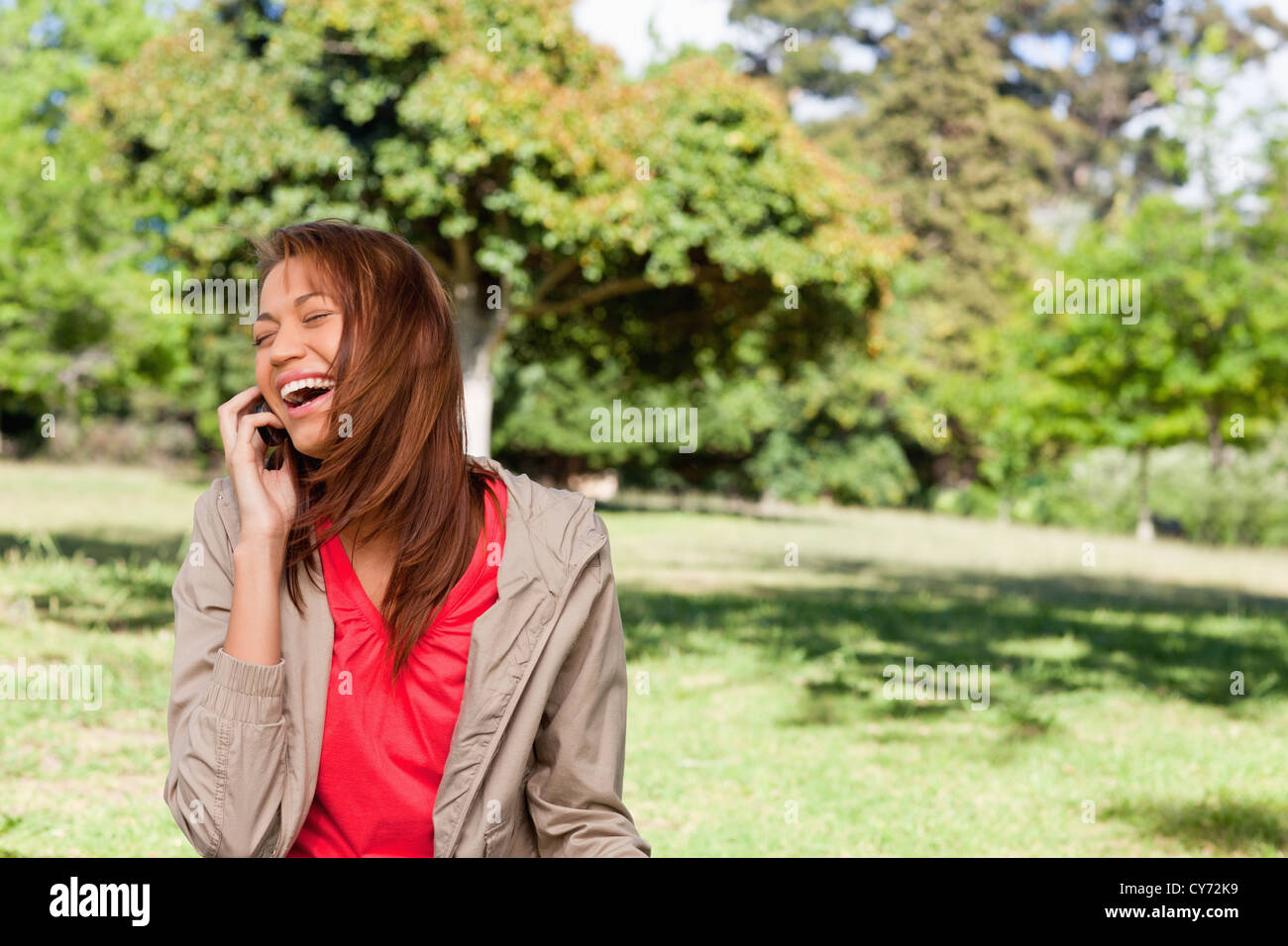 Young woman enthusiastically laughing while on the phone in an open grassland area Stock Photo