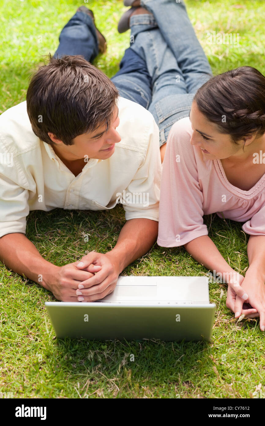 Two friends looking at each other as they lie down with a laptop Stock Photo