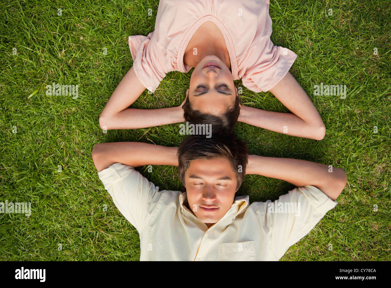 Forehead Rests Against Another Woman and a man lying head to head with both hands behind their neck ...