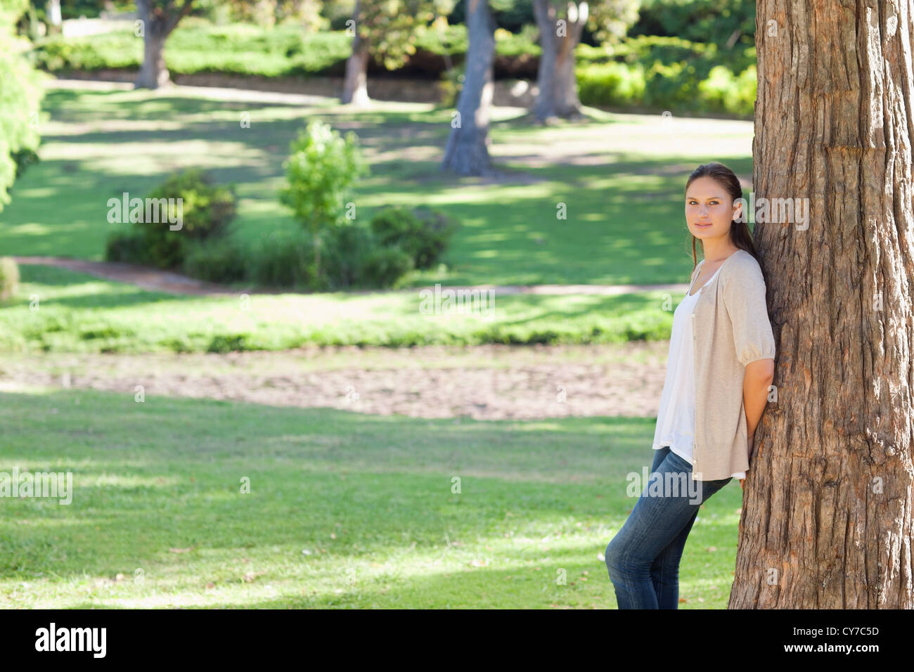 Woman leaning against a tree in the park Stock Photo - Alamy