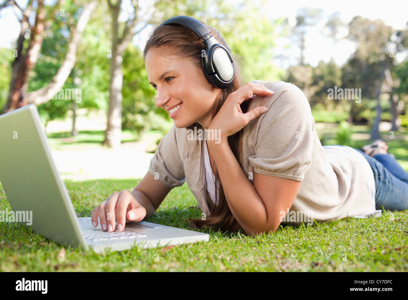 Woman with a laptop and a headset lying on the lawn Stock Photo - Alamy