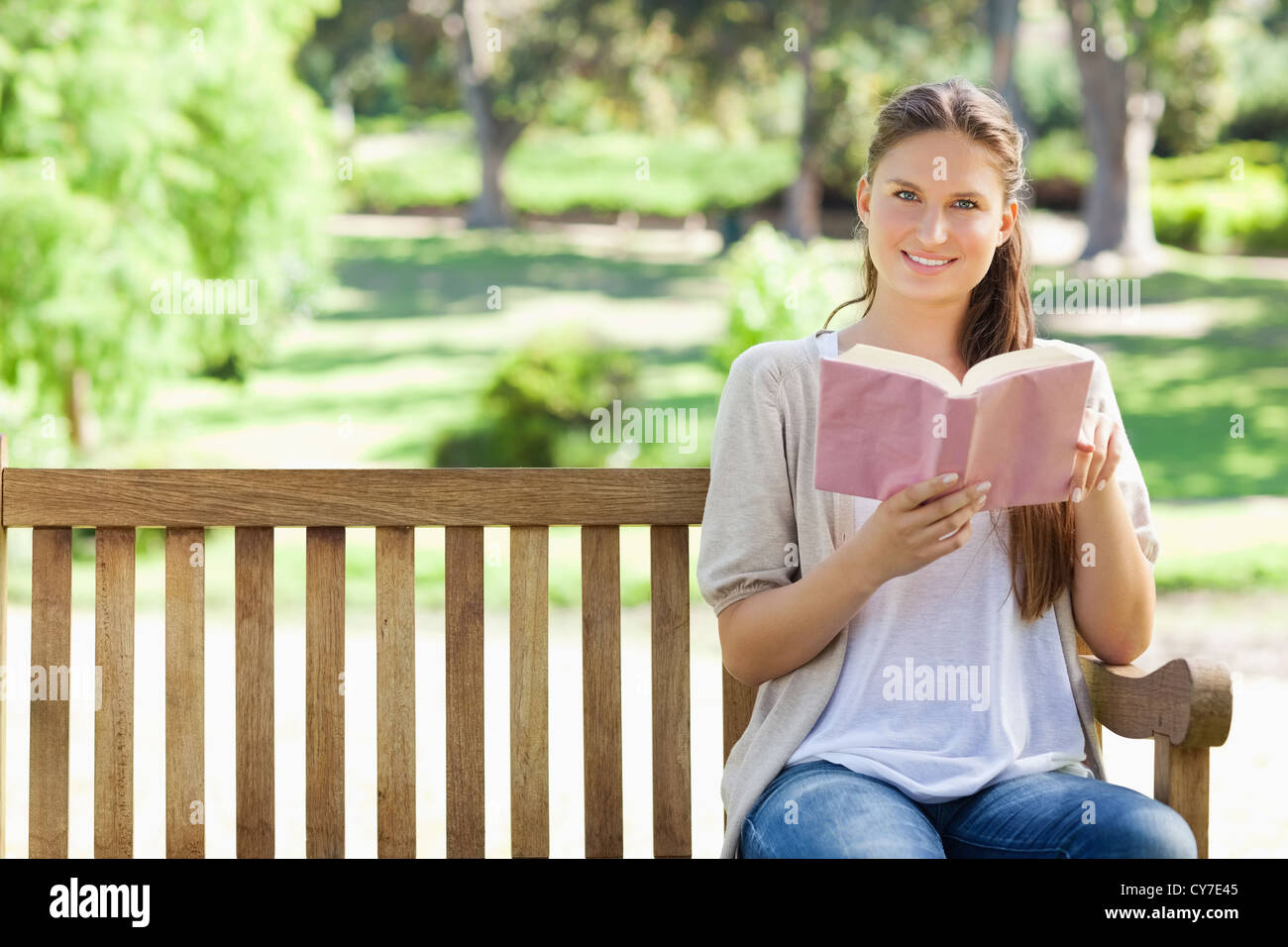 Woman sitting with a book on a park bench Stock Photo - Alamy