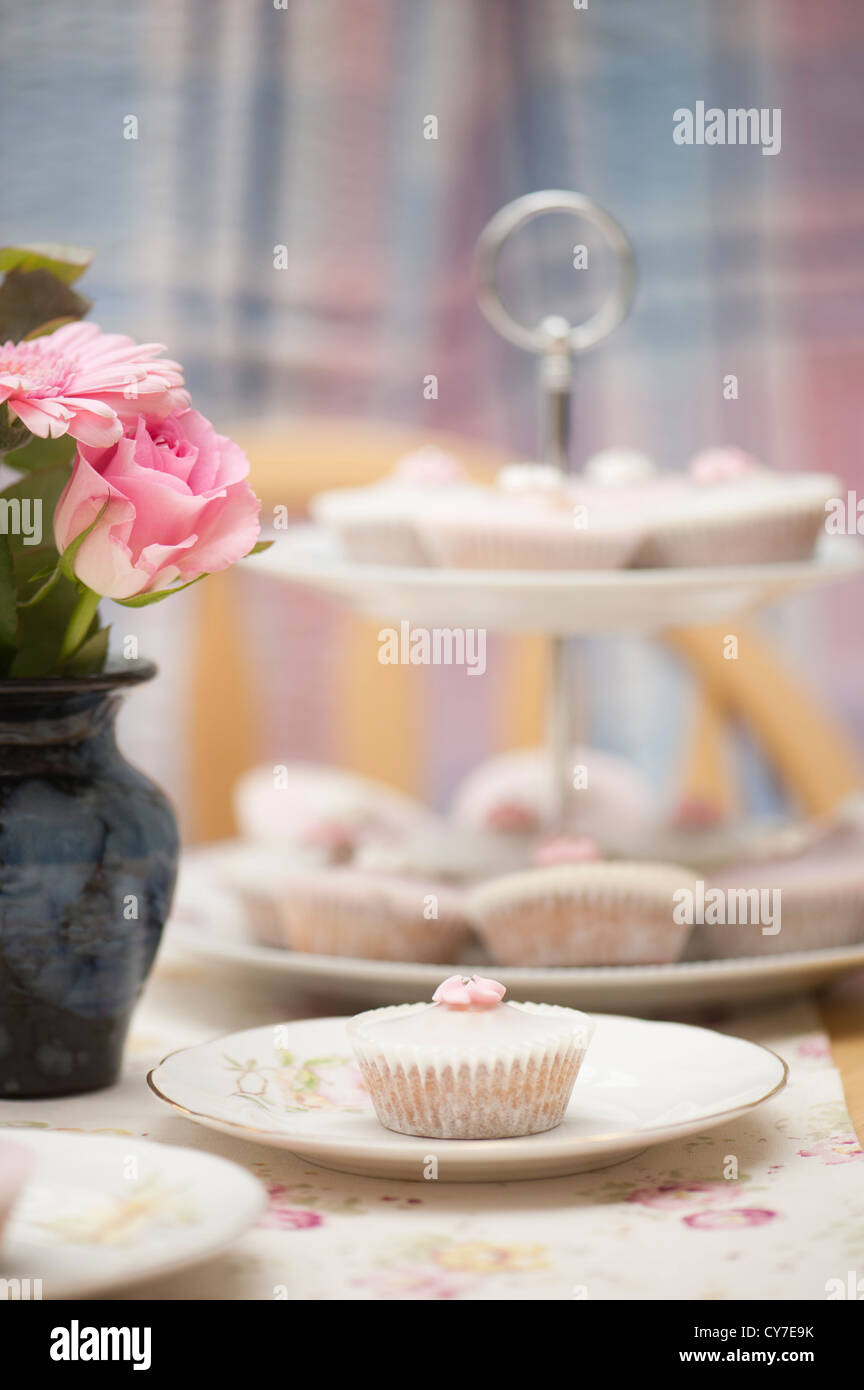 Pink and white fairy cakes with a posy of pink flowers Stock Photo