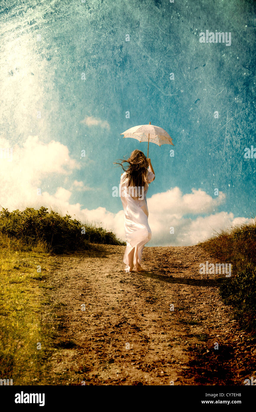 a girl in a white dress is walking in the dunes with a parasol Stock Photo