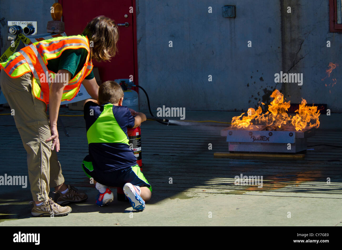 Cert person showing young lad how to use a fire extinguisher. Stock Photo