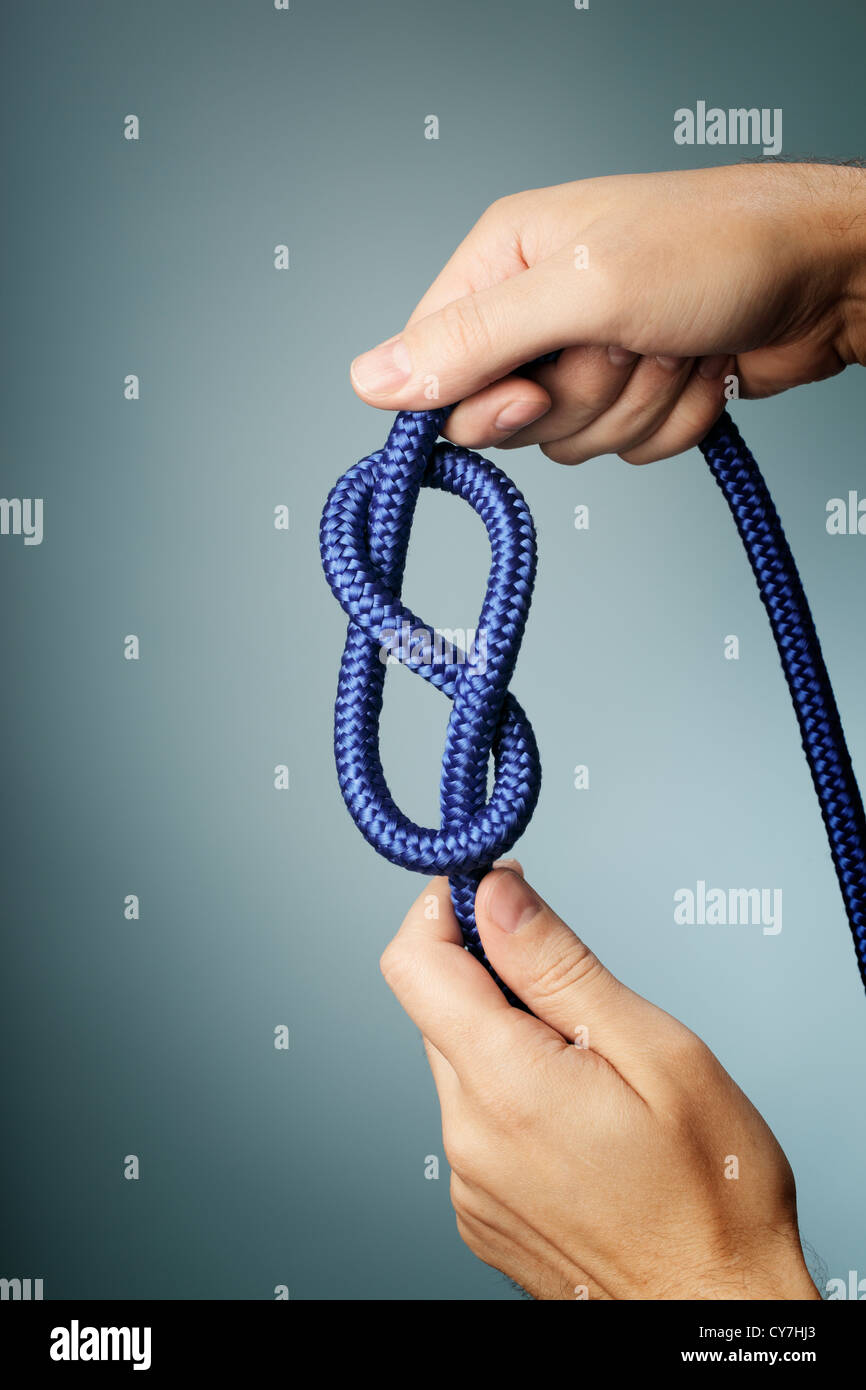 Man holding blue rope with figure of eight knot in his hands. Stock Photo