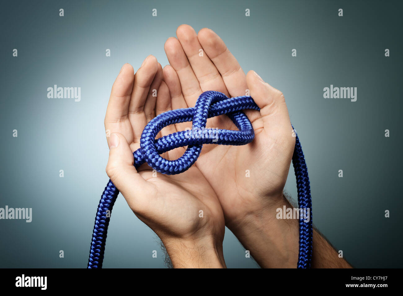 Man holding a blue rope with a figure of eight knot in his hands. Stock Photo