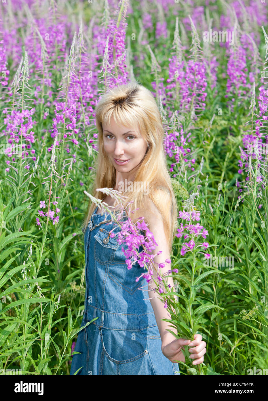 The smiling young woman with bunch of willowherb flower in the field Stock Photo