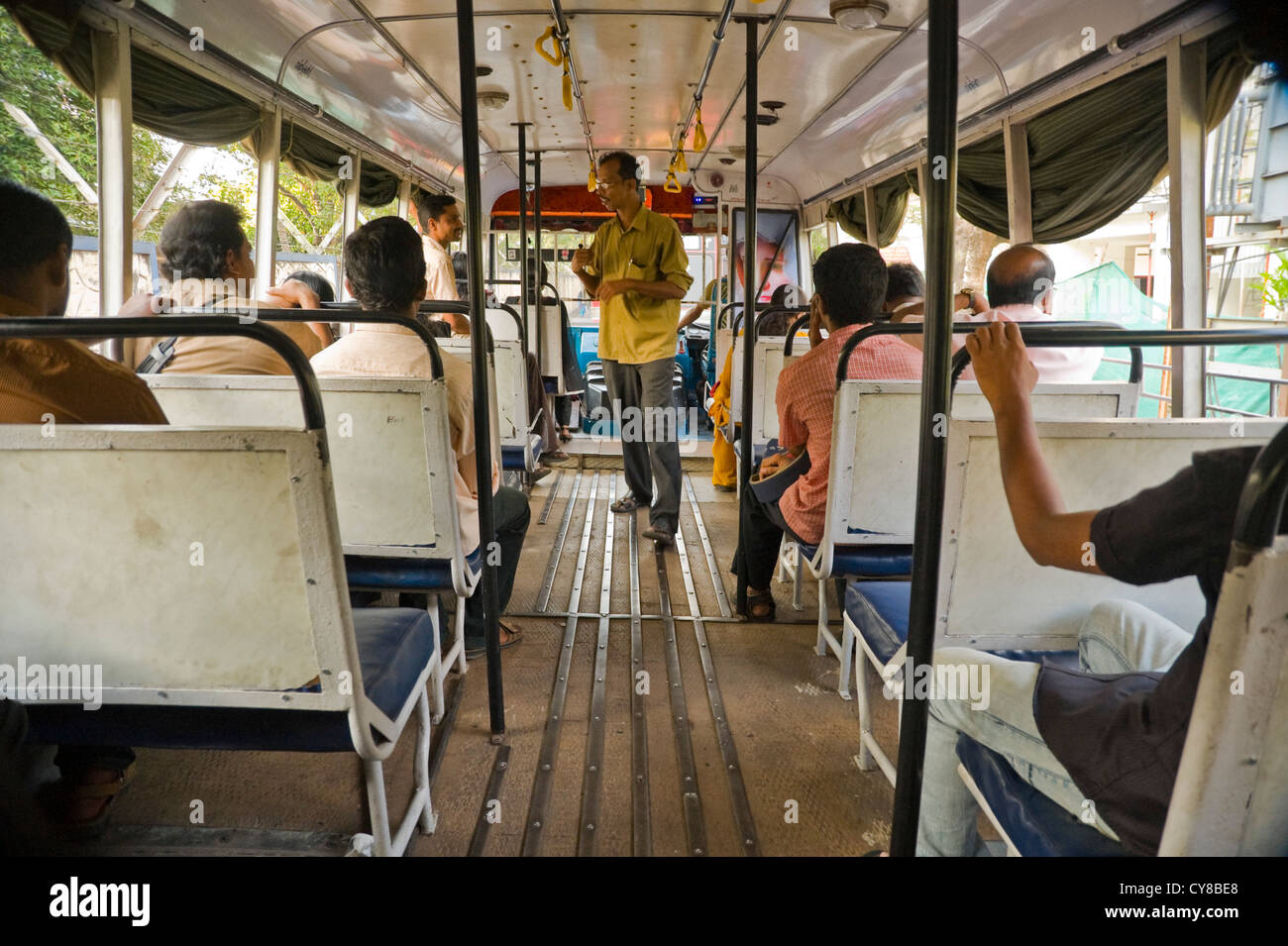 Horizontal interior view of a public bus in Kerala with a conductor collecting fares. Stock Photo