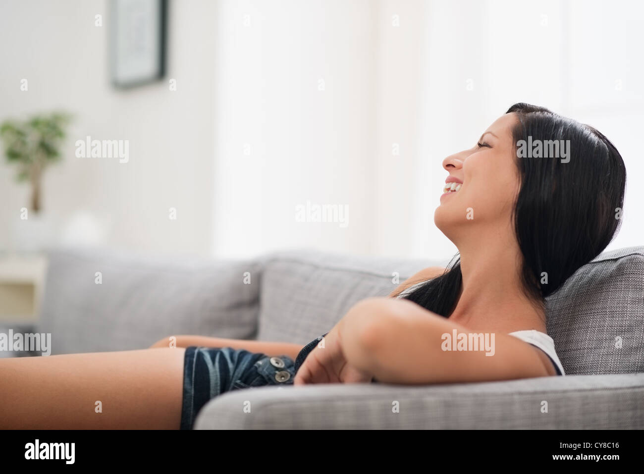 Smiling young woman laying on sofa Stock Photo