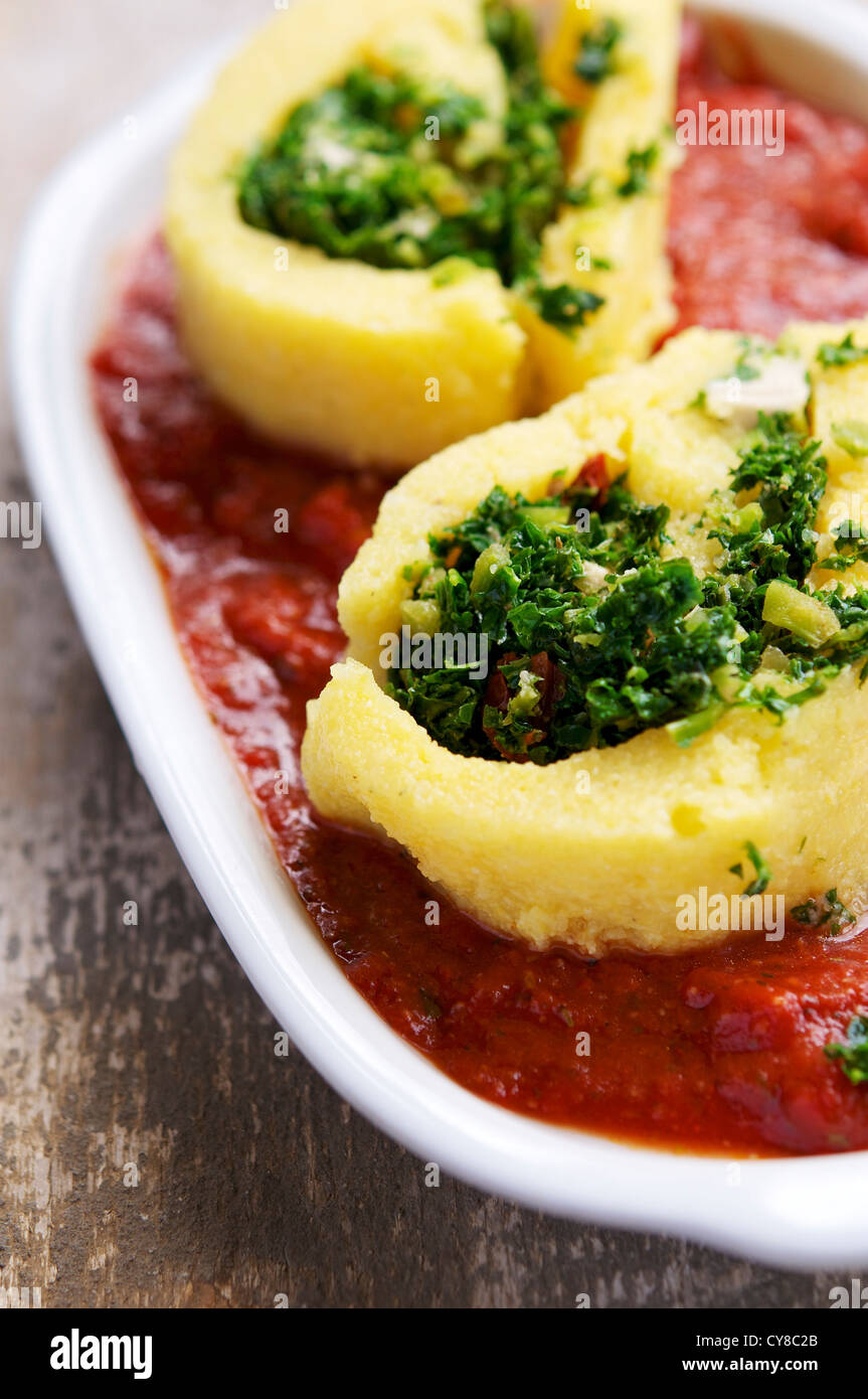 A roulade made from polenta and filled with kale, served on tomato sauce. Stock Photo