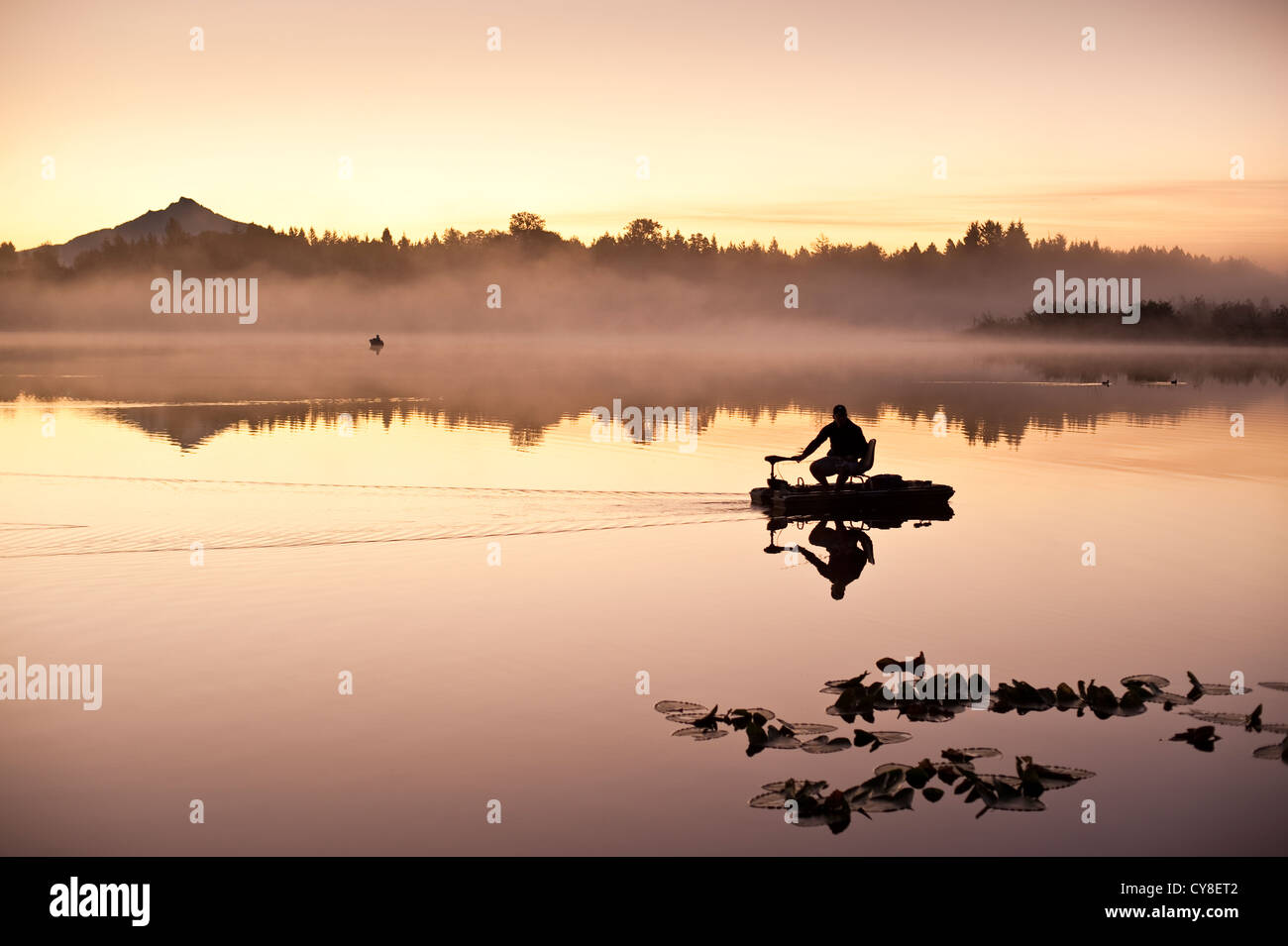 Sunrise in fog Lake Cassidy with fishermen in small fishing boat Stock