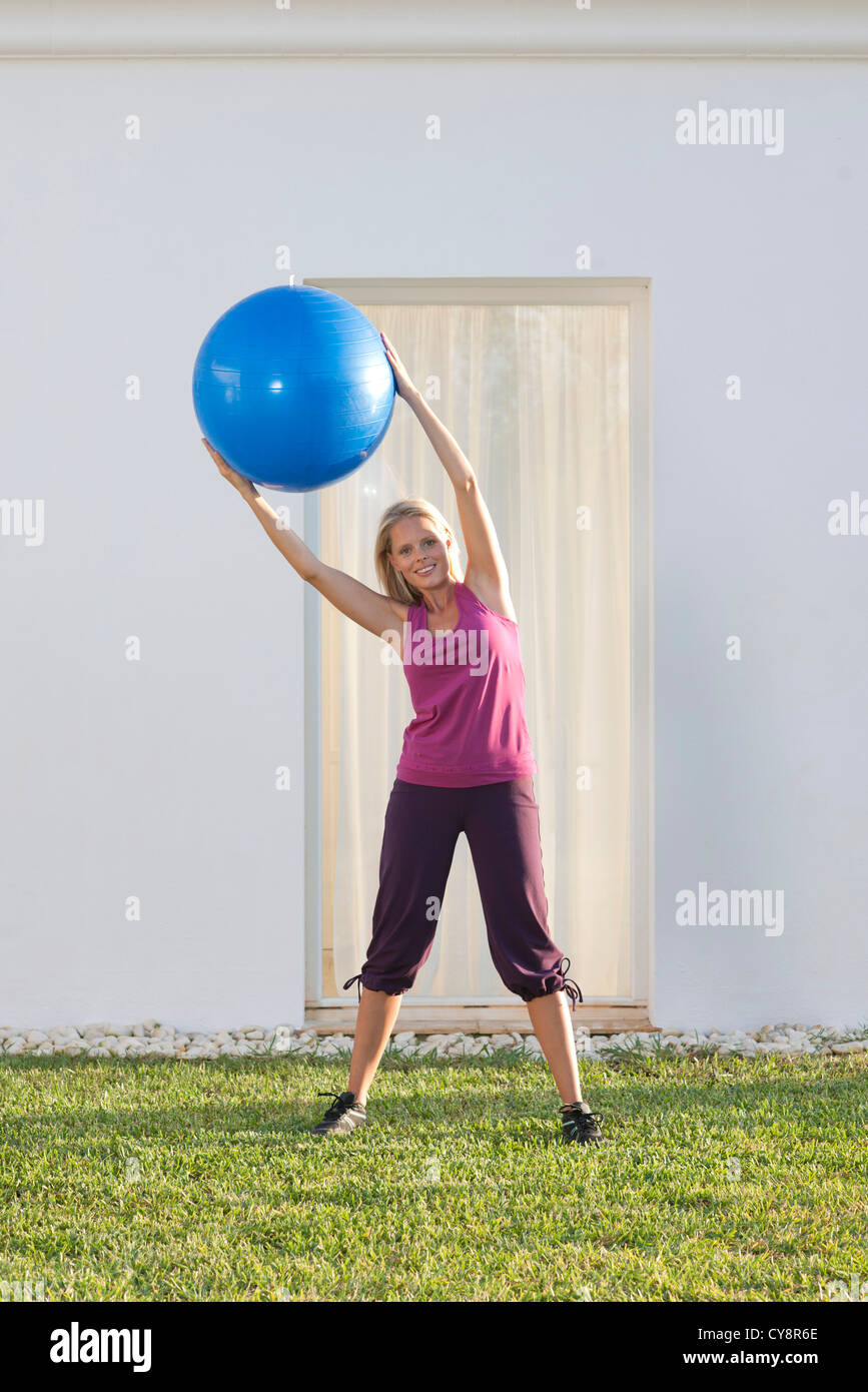 Young woman holding up fitness ball, leaning to one side Stock Photo
