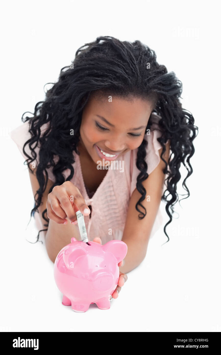 A young woman lying on the floor is putting money into a piggy bank ...