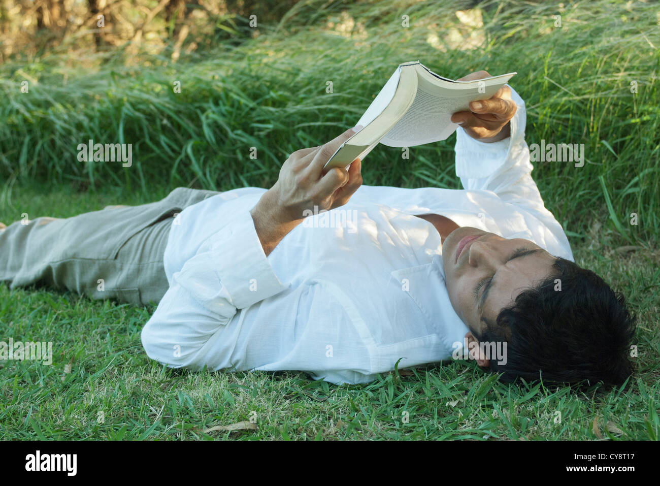 Mid-adult man lying on grass reading book Stock Photo