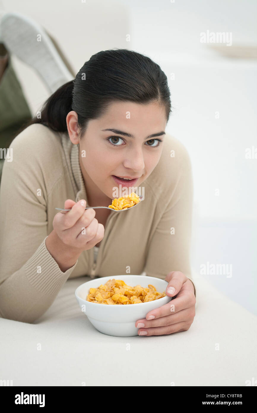 Young woman lying on stomach, eating bowl of cereal Stock Photo Alamy
