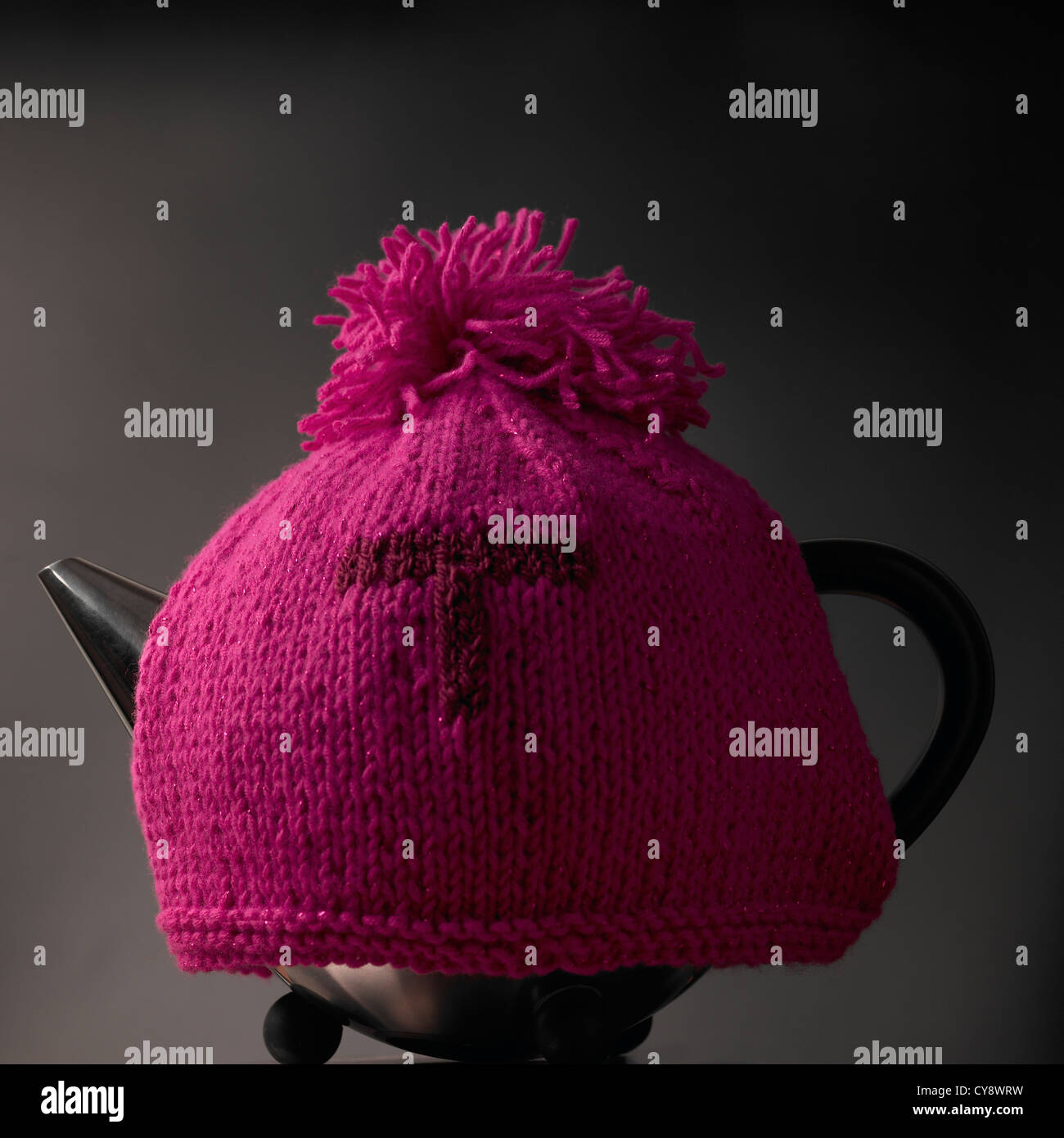 Contemporary teapot and traditional knitted pink woollen tea cosy with letter T Stock Photo