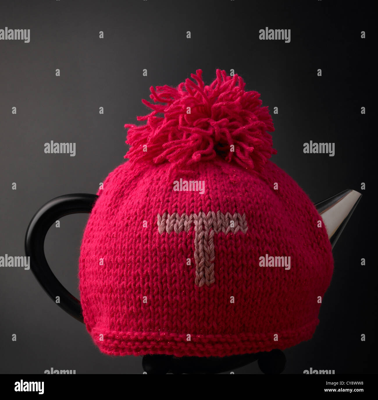 Contemporary teapot and traditional knitted red woollen tea cosy with letter T Stock Photo