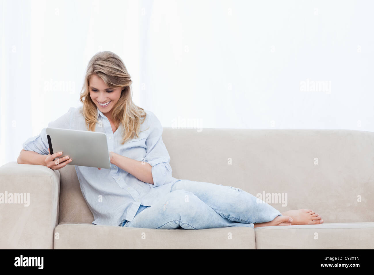 A smiling woman holding a tablet is sitting on a couch Stock Photo - Alamy