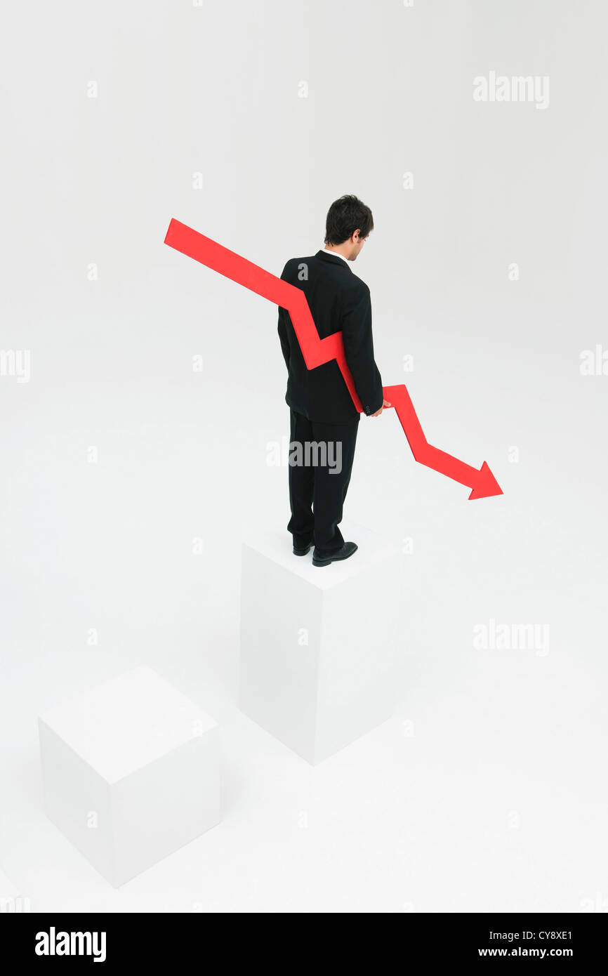 Businessman standing at top of steps holding arrow pointed downward Stock Photo