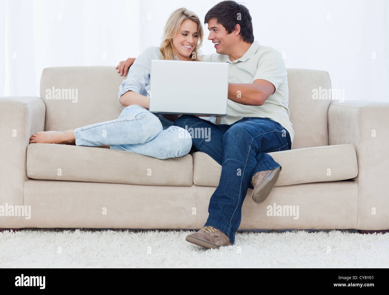 A young couple sitting on a couch with a laptop Stock Photo - Alamy