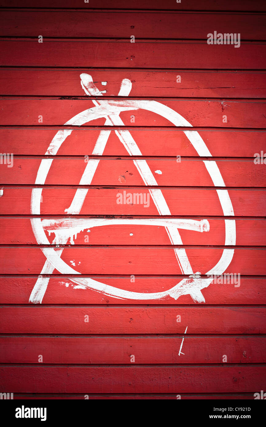 Anarchy sign painted on red wall in white color. Stock Photo