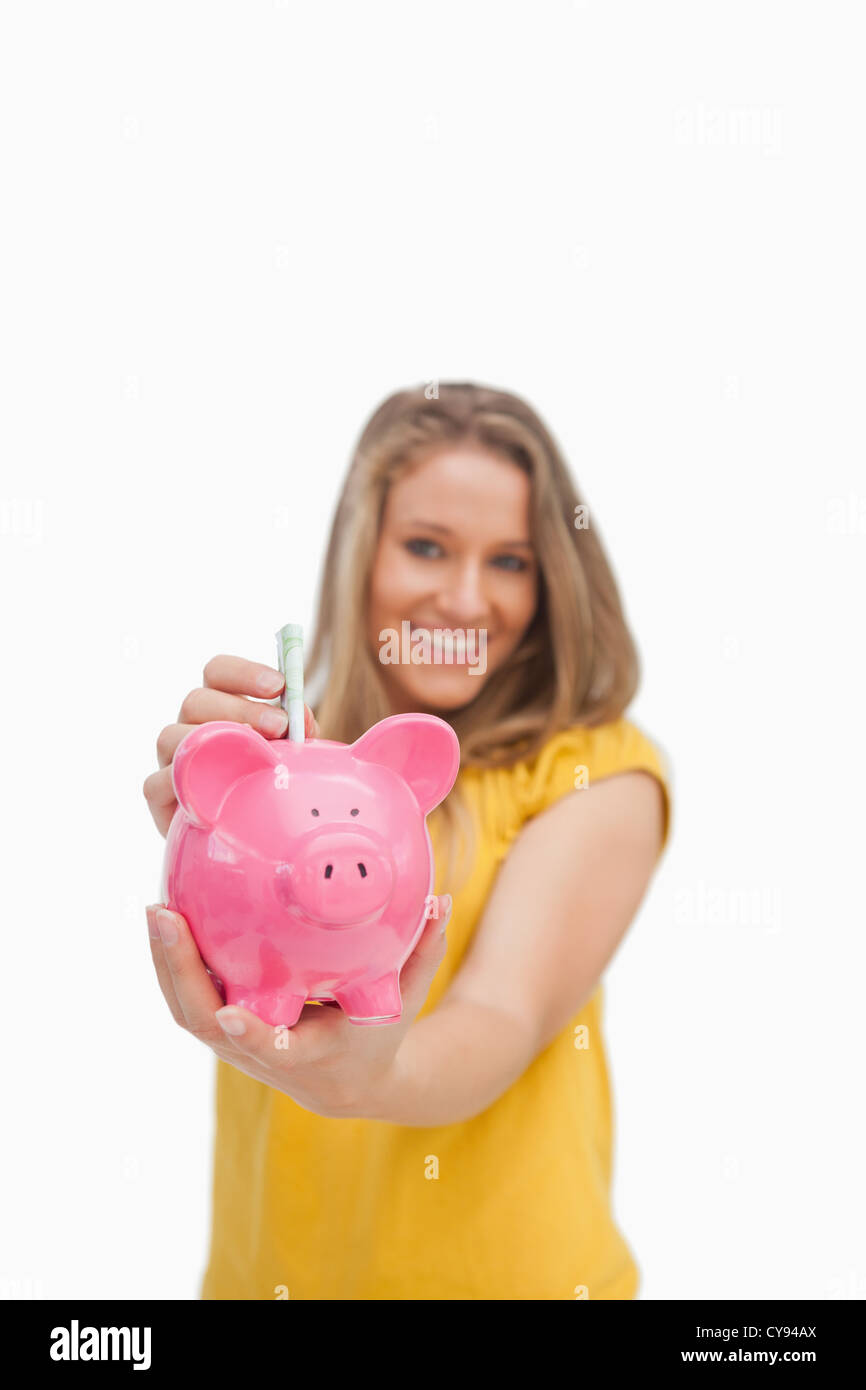 Young blond woman putting money into a piggy-bank Stock Photo - Alamy