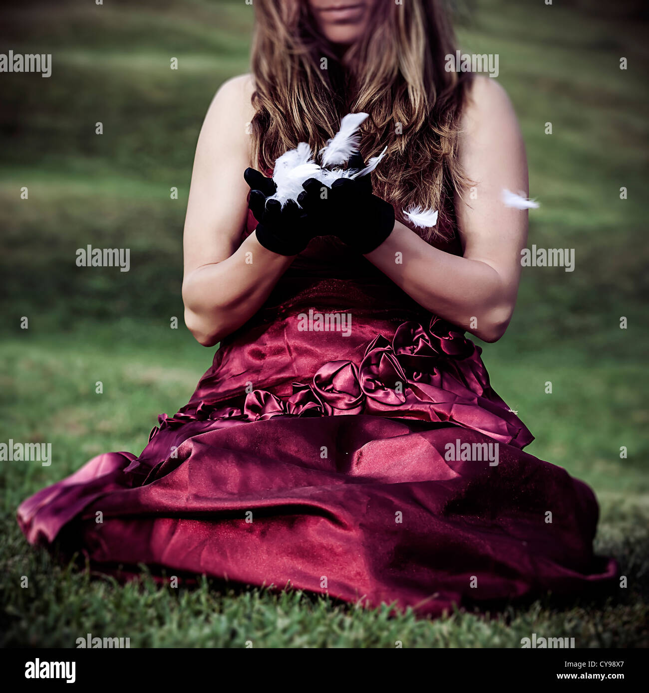 a woman in a red dress is sitting on a meadow, holding feathers in her ...