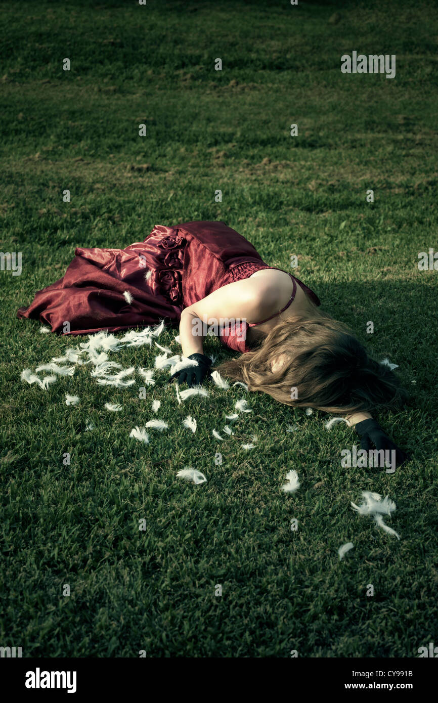 a woman in a red dress is lying on a meadow amongst feathers Stock Photo