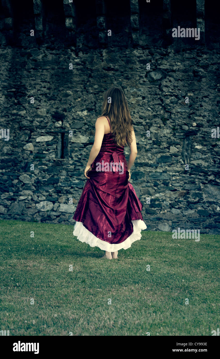 a woman in a red dress is running at a castle wall Stock Photo
