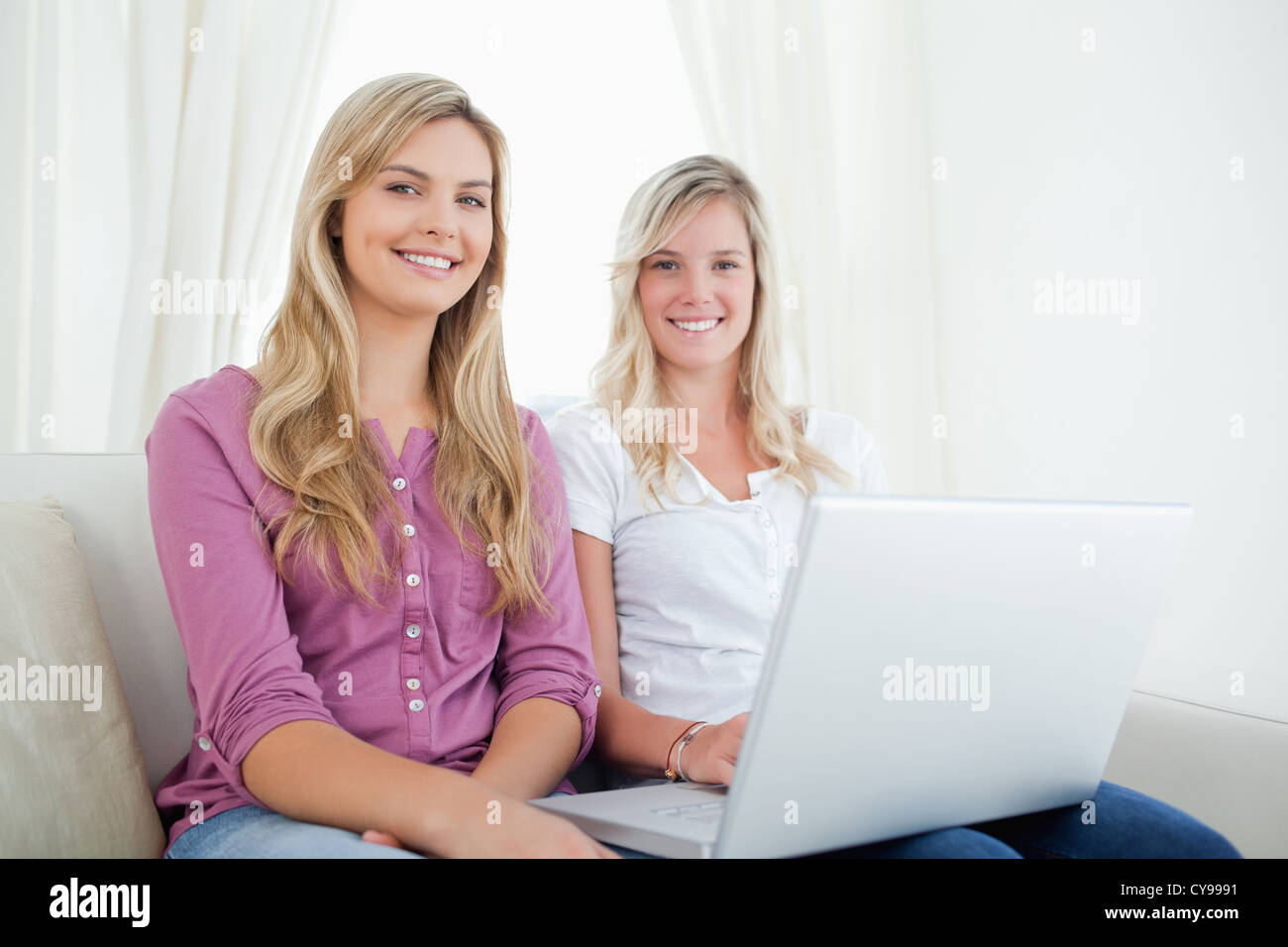 Sisters sitting on the couch looking at the camera as they hold a ...