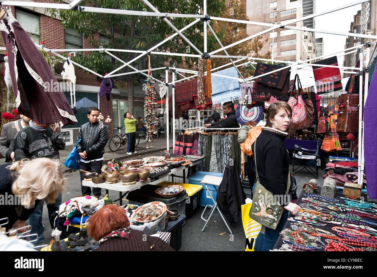 diverse people shoppers browse crowded booth featuring craft items & clothing for sale at Hells Kitchen weekend flea market Stock Photo