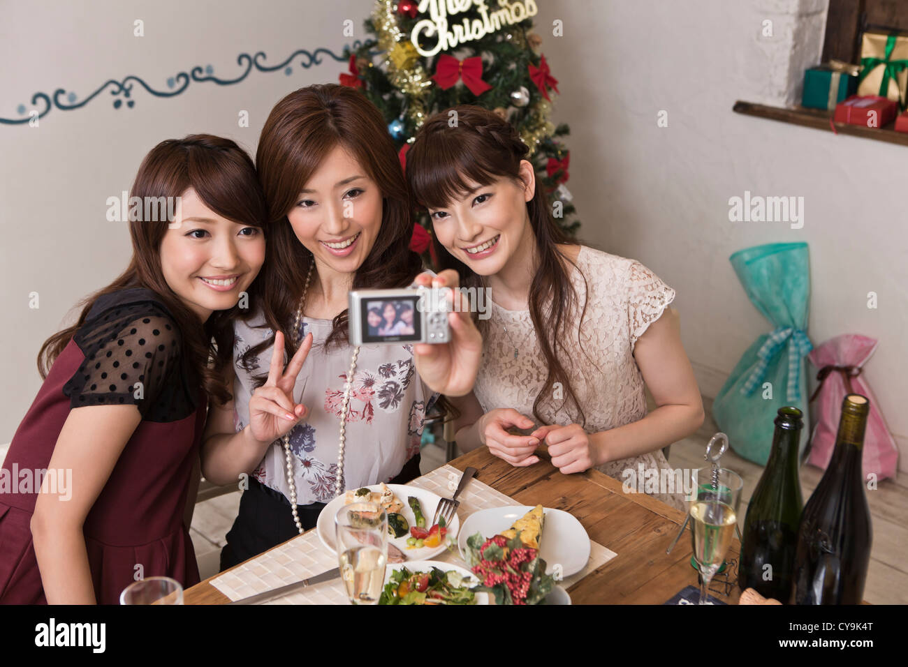 Three Young Women Taking Photograph with Digital Camera at Christmas Party Stock Photo