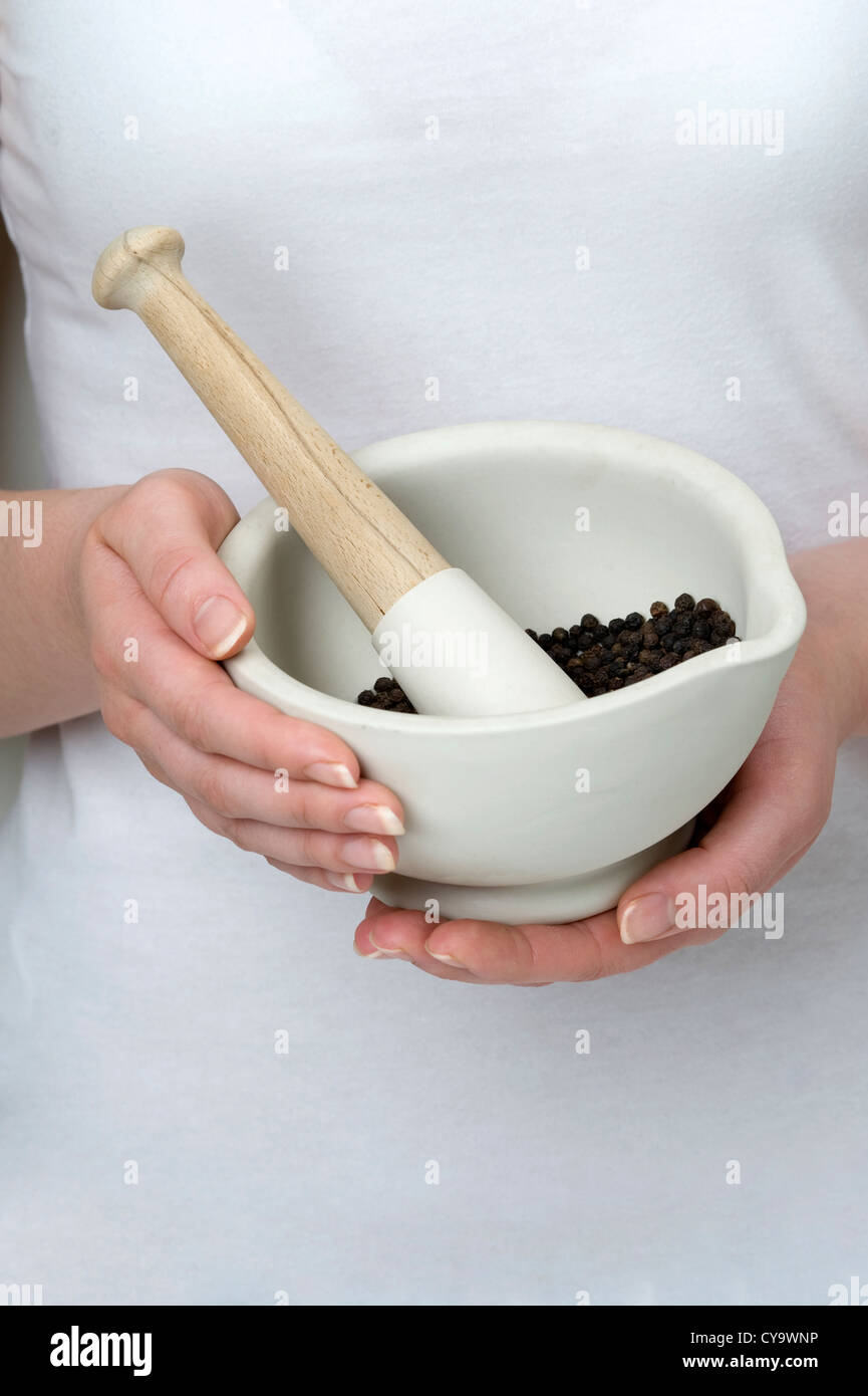woman holding pestle and mortar with black peppercorns Stock Photo