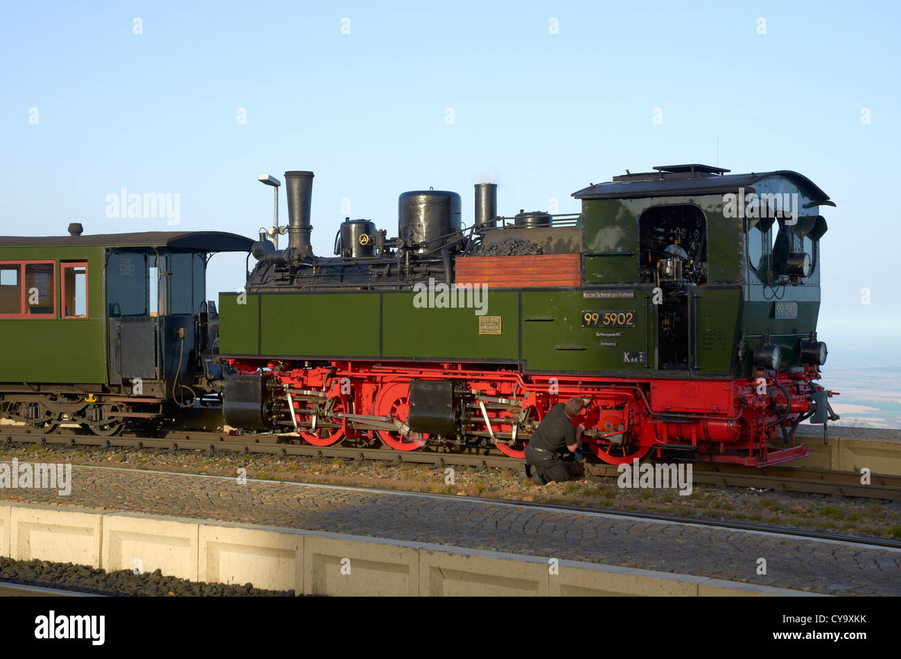 Harzer Schmalspurbahnen heritage steam train standing at Brocken station. Firemen cleaning wheels and motion. Stock Photo