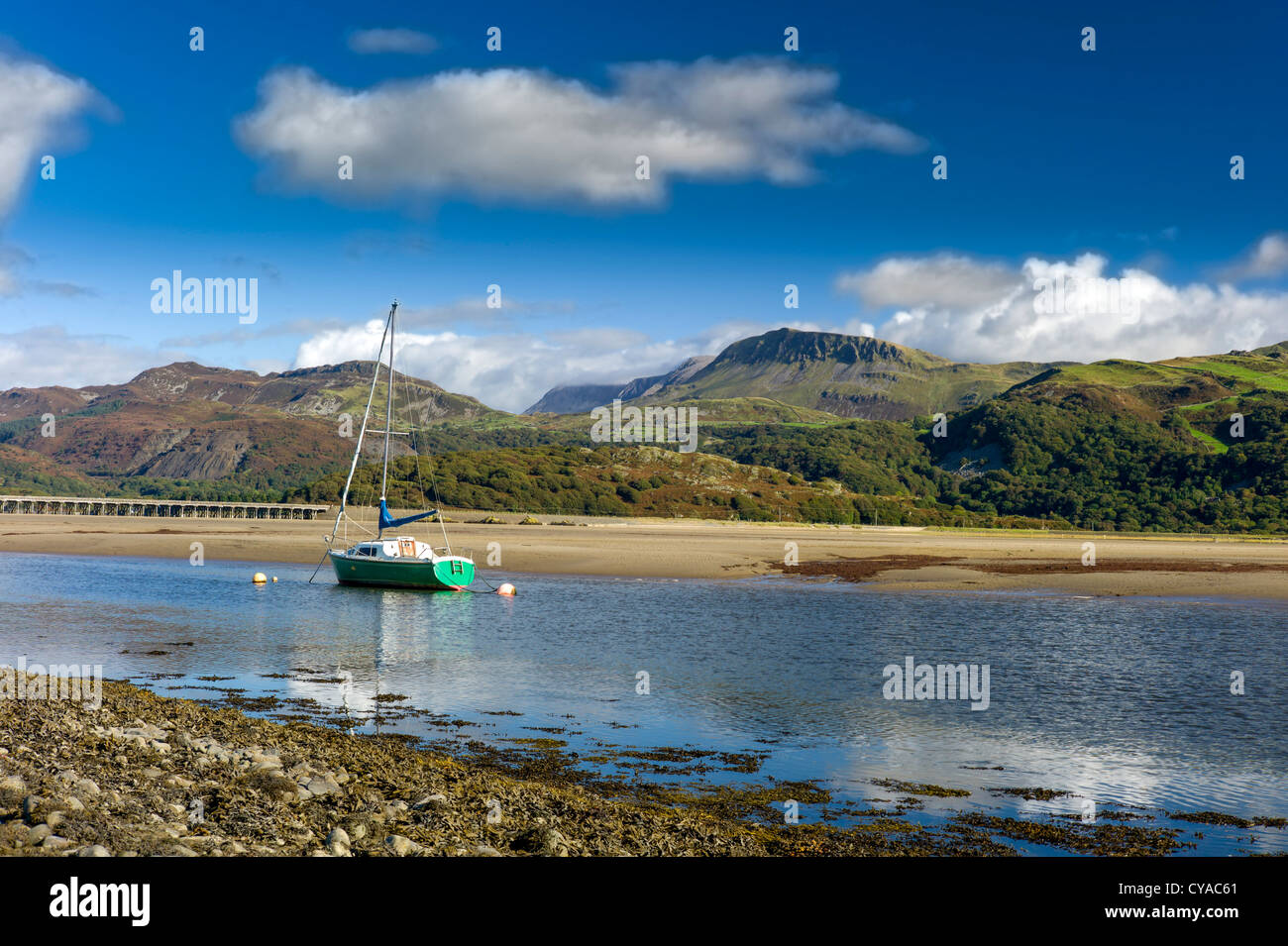 A green hulled sailing yacht is anchored in the mawddach estuary, low tide, cadair idris mountains in background, peaceful, sun Stock Photo